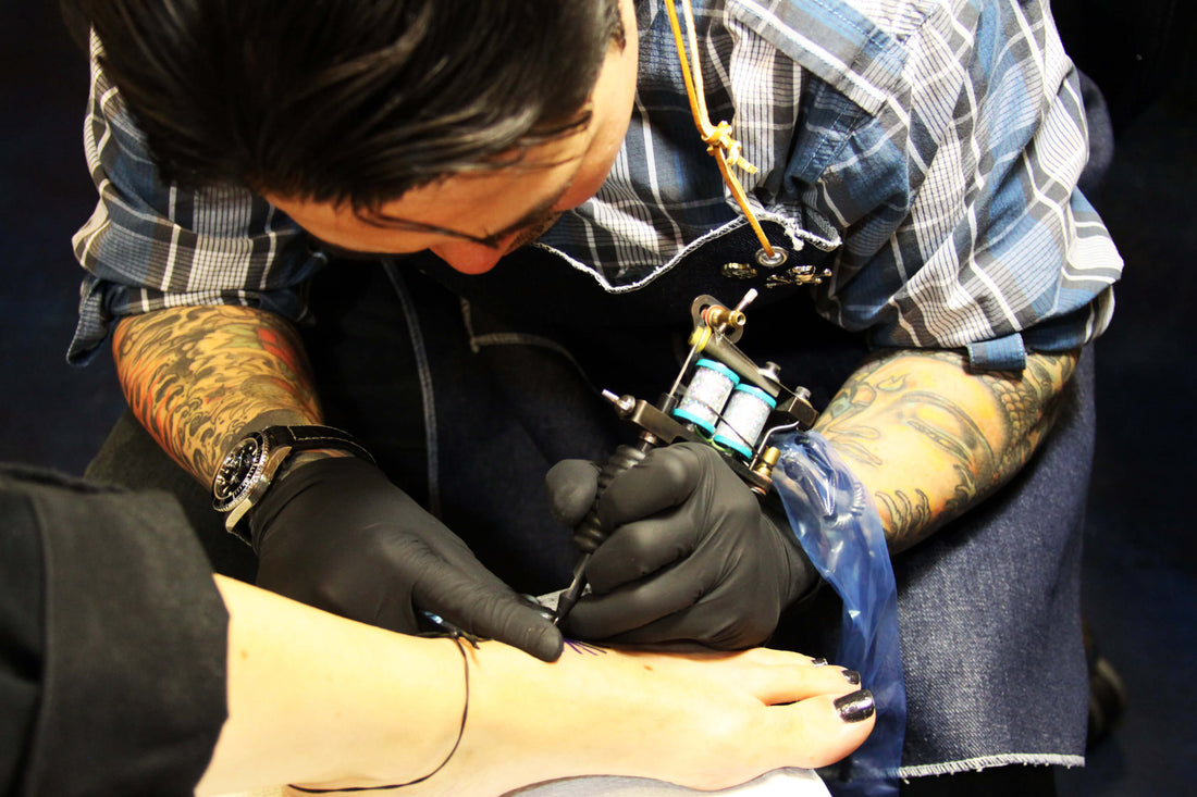 artist tattooing on foot